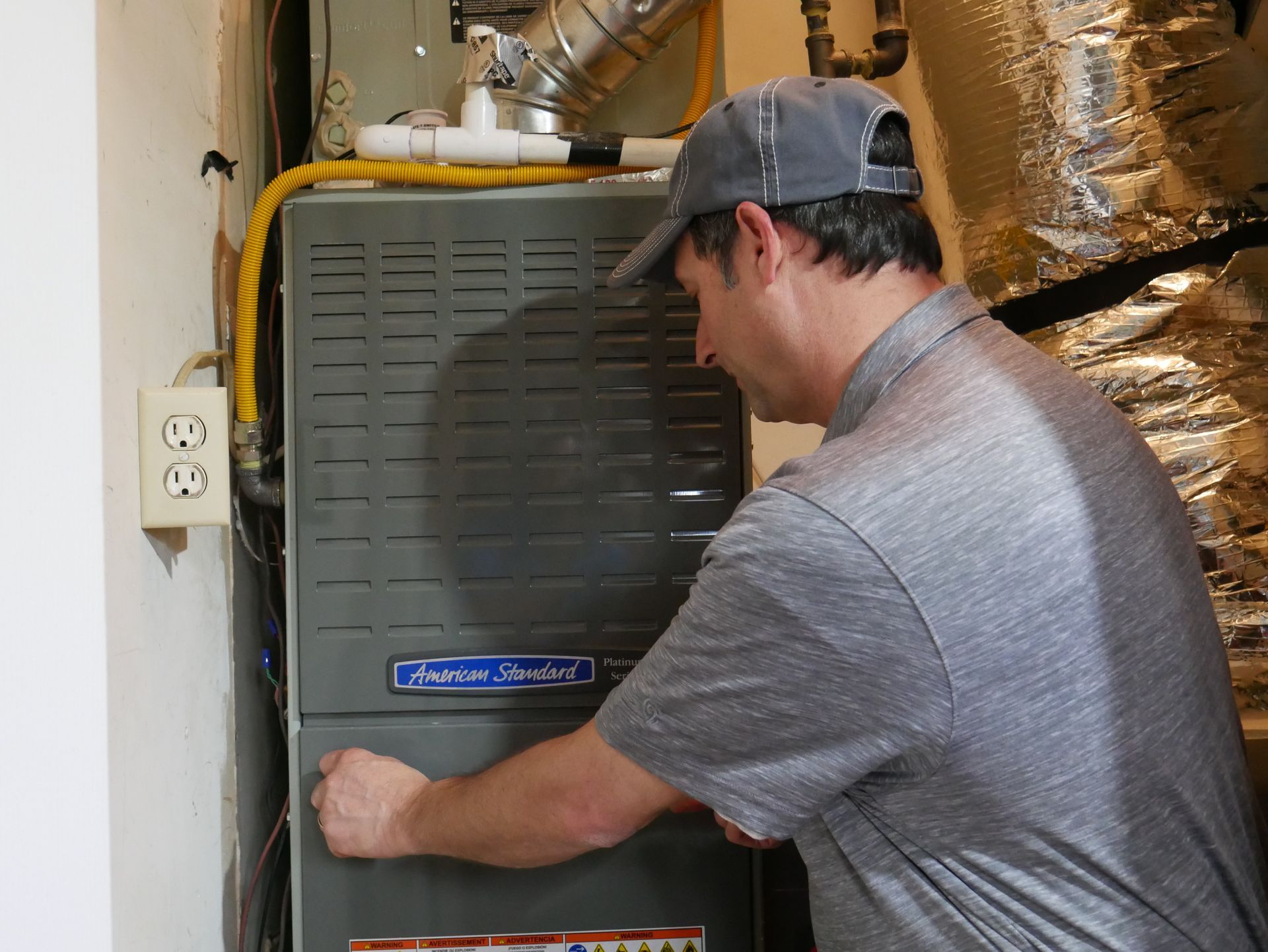 A man is working on an air conditioner in a basement.