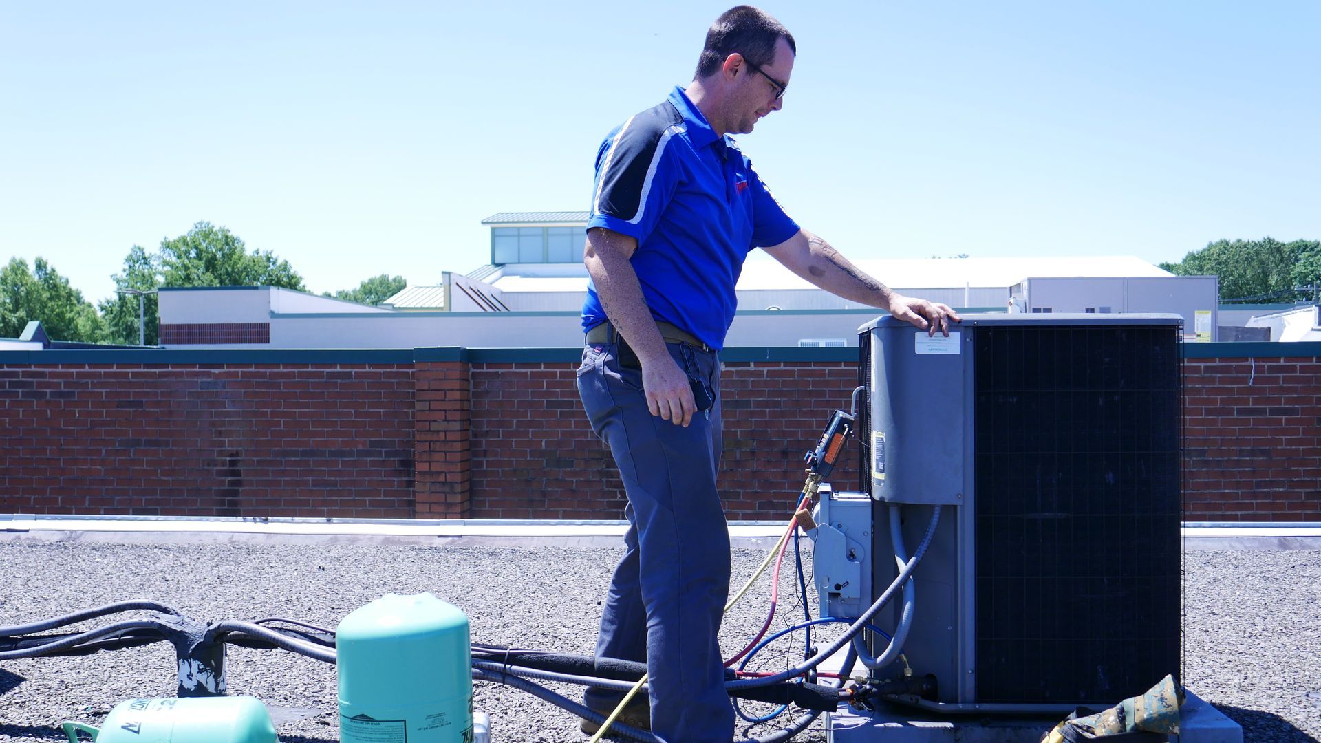 A man is working on an air conditioner on the roof of a building.