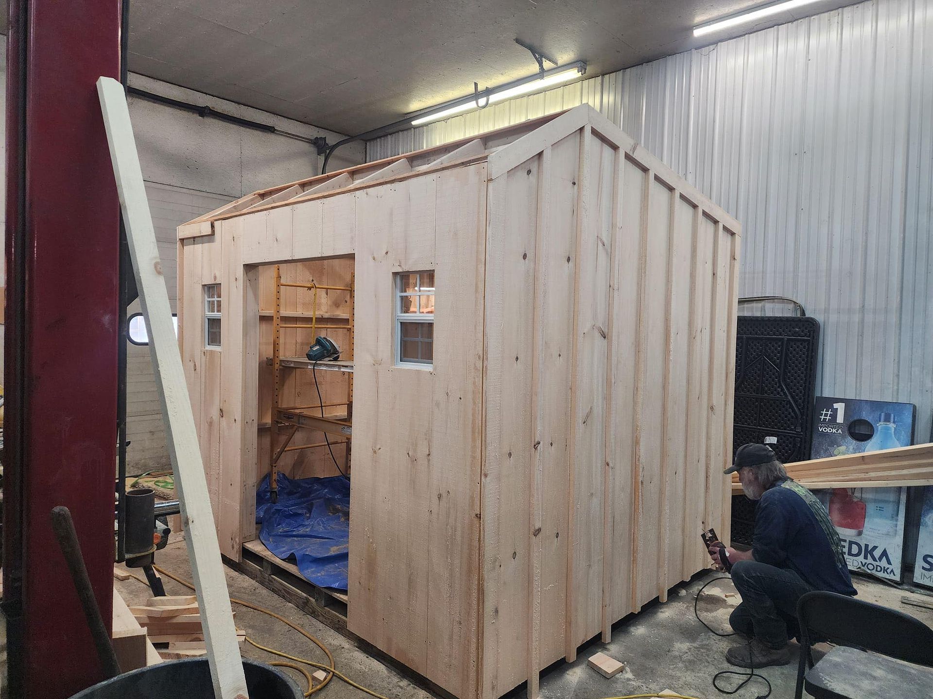 A man is working on a wooden shed in a garage.