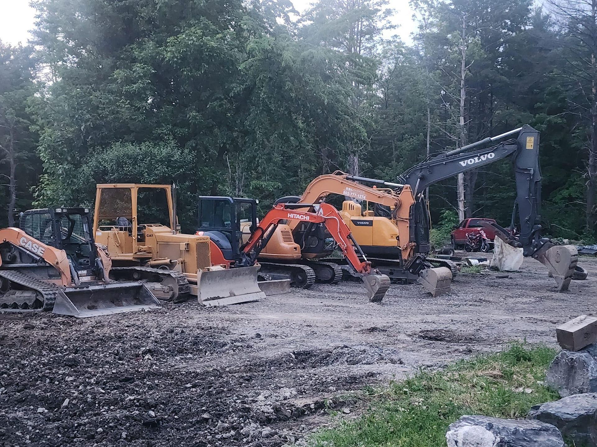 A group of construction vehicles are parked in a dirt field.
