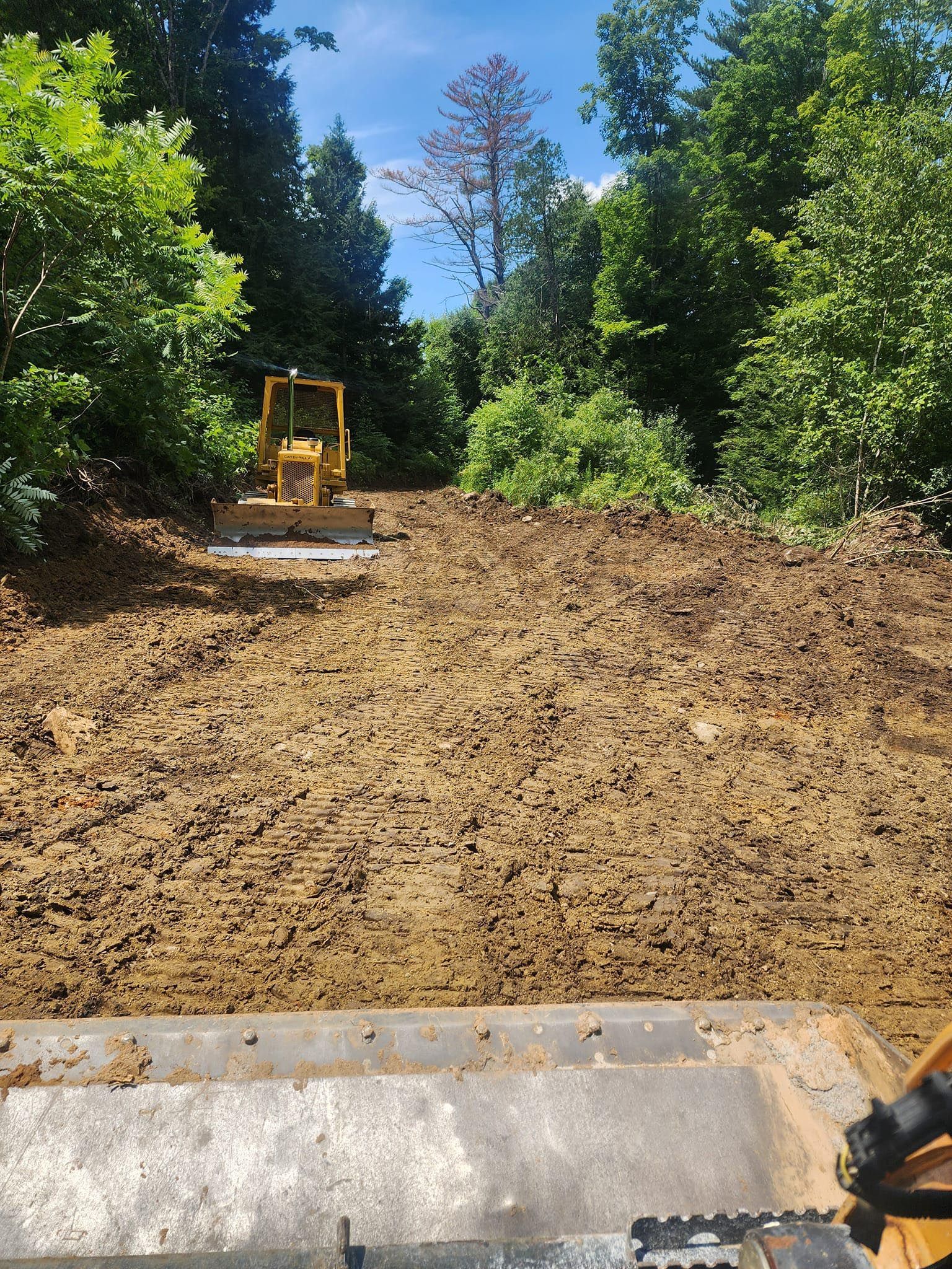 A bulldozer is moving dirt in a field with trees in the background.