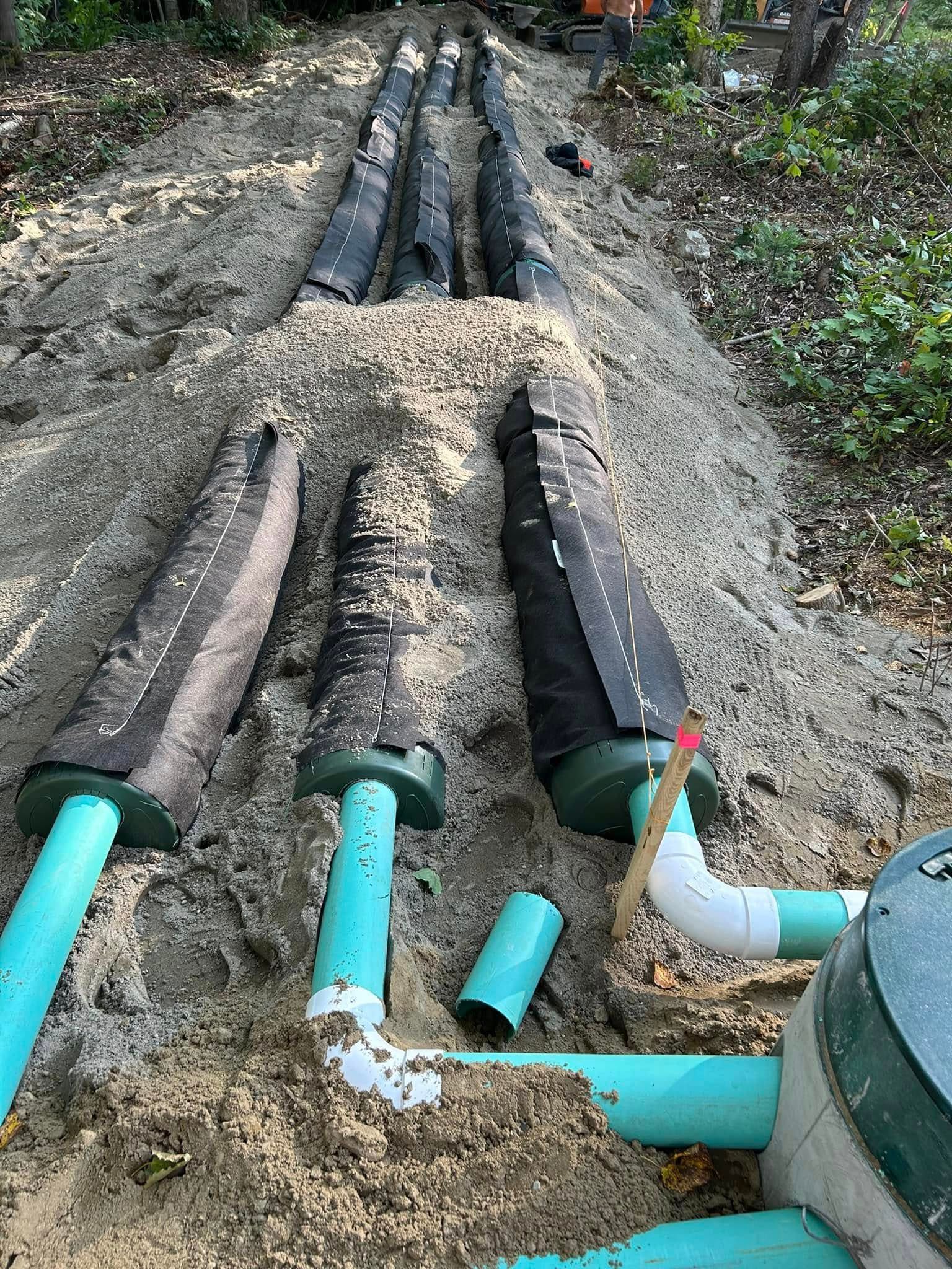 A bunch of pipes are laying in the dirt.