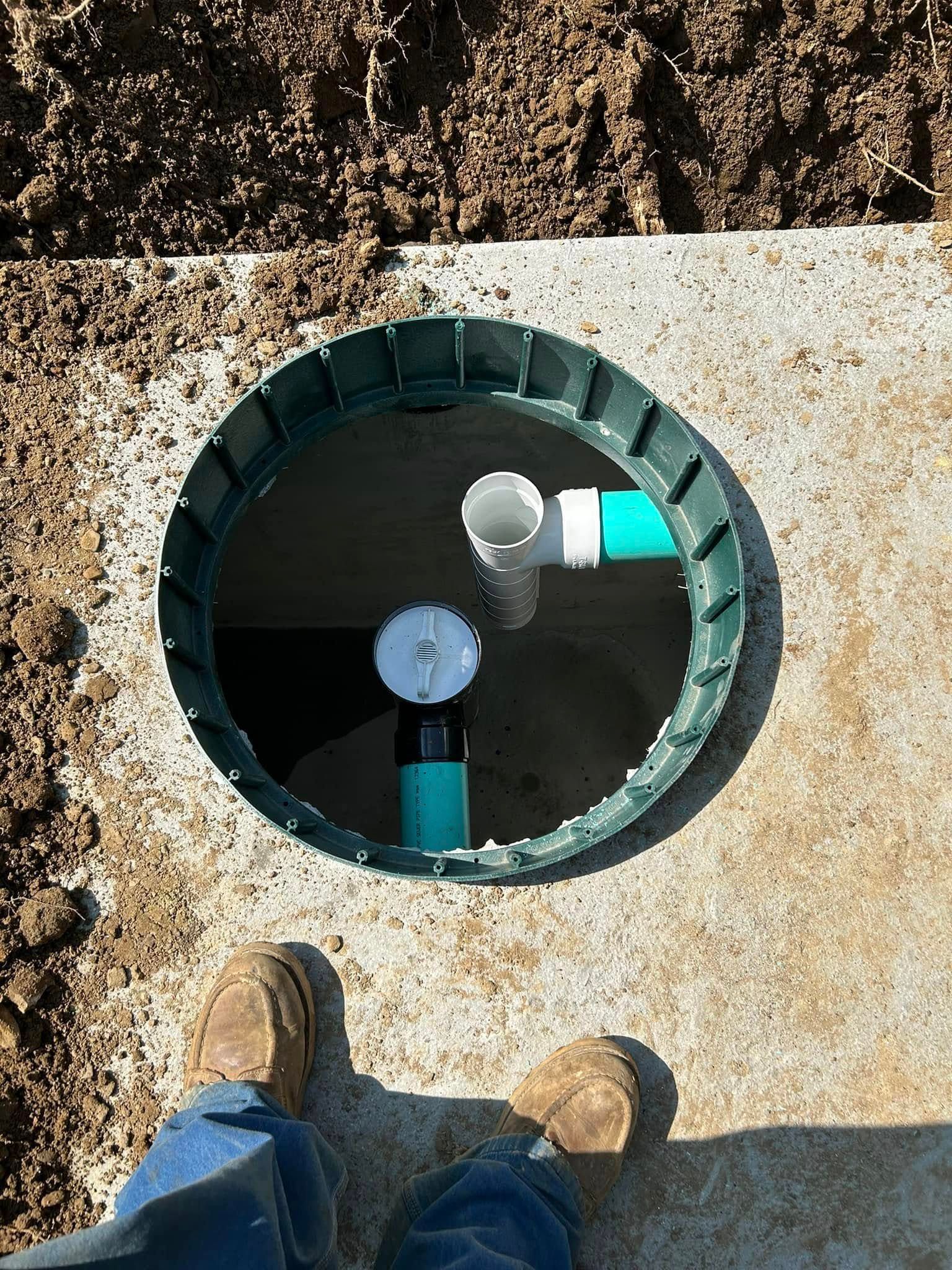 A person is standing next to a hole in the ground with pipes in it.