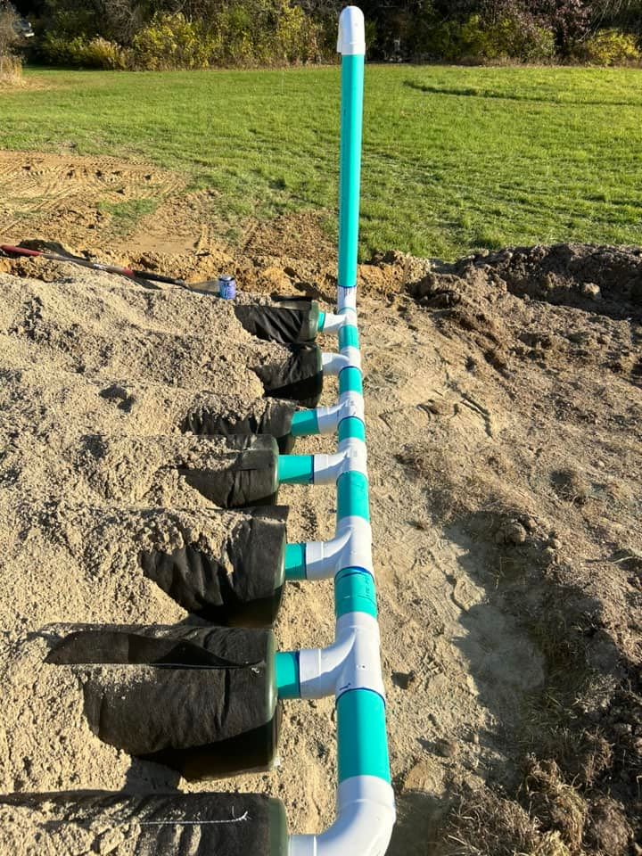 A row of green and white pipes are sitting in the dirt.