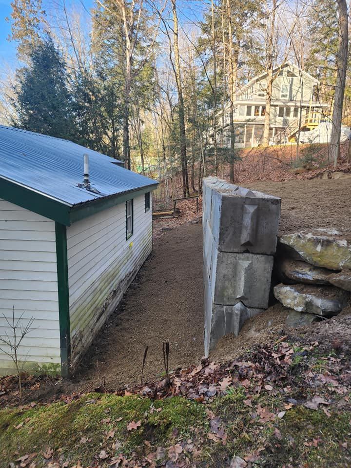 A white house with a green trim is sitting next to a large rock wall.