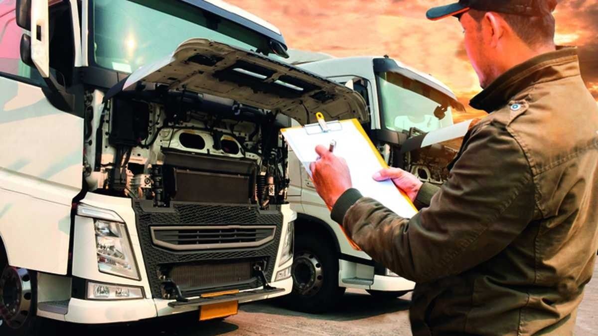 Hombre inspeccionando el motor del camión, sosteniendo un portapapeles, al aire libre con otros camiones.