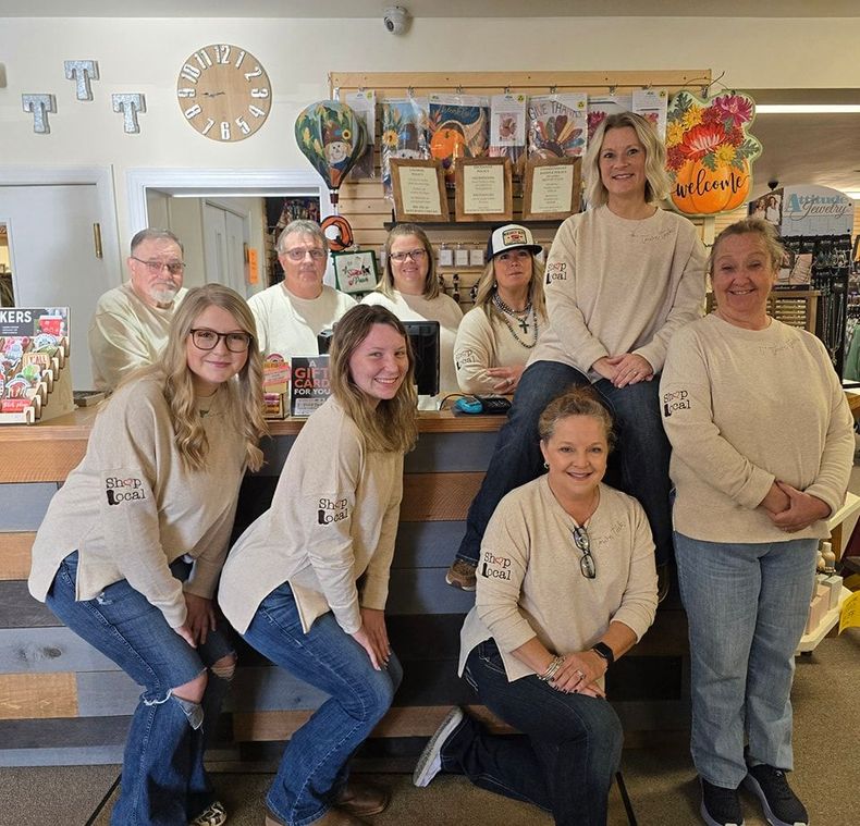 A group of people in tan shirts and jeans pose behind a store counter.