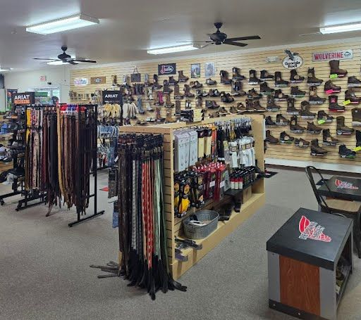 Interior of a retail store; boots on display, belts and accessories on racks, a register and branded display.