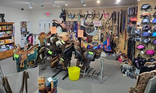 Inside of a tack shop, various saddles, gear, and helmets are displayed for sale.
