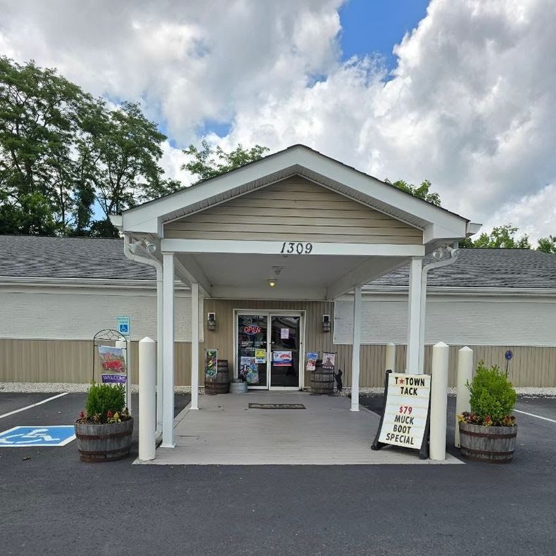 Entrance to a small store with a covered porch, sign for a sale, and a handicap parking space.