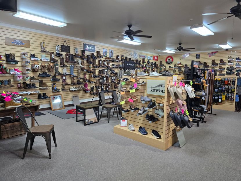 Shoe store interior with rows of shoes displayed on shelves and racks, chairs, and ceiling fans.