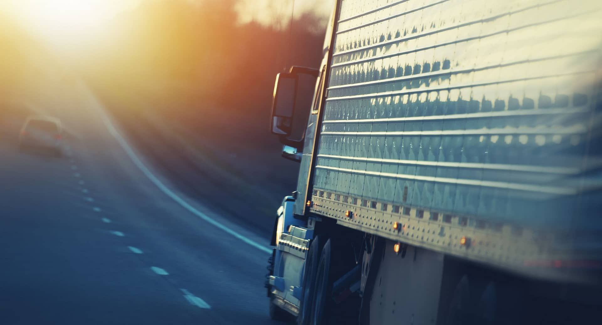 A semi truck is driving down a highway at sunset.