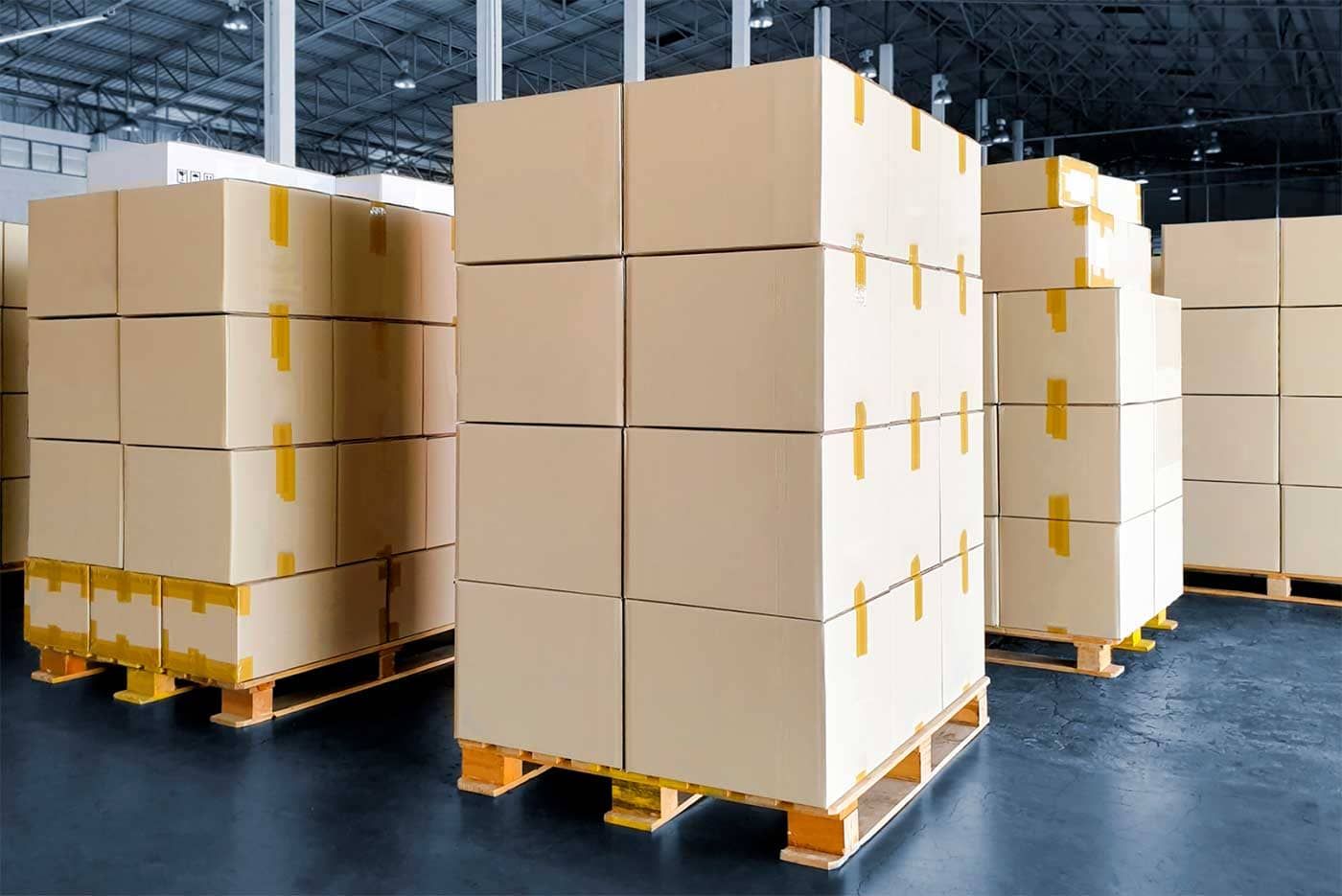 A warehouse filled with lots of cardboard boxes on wooden pallets.