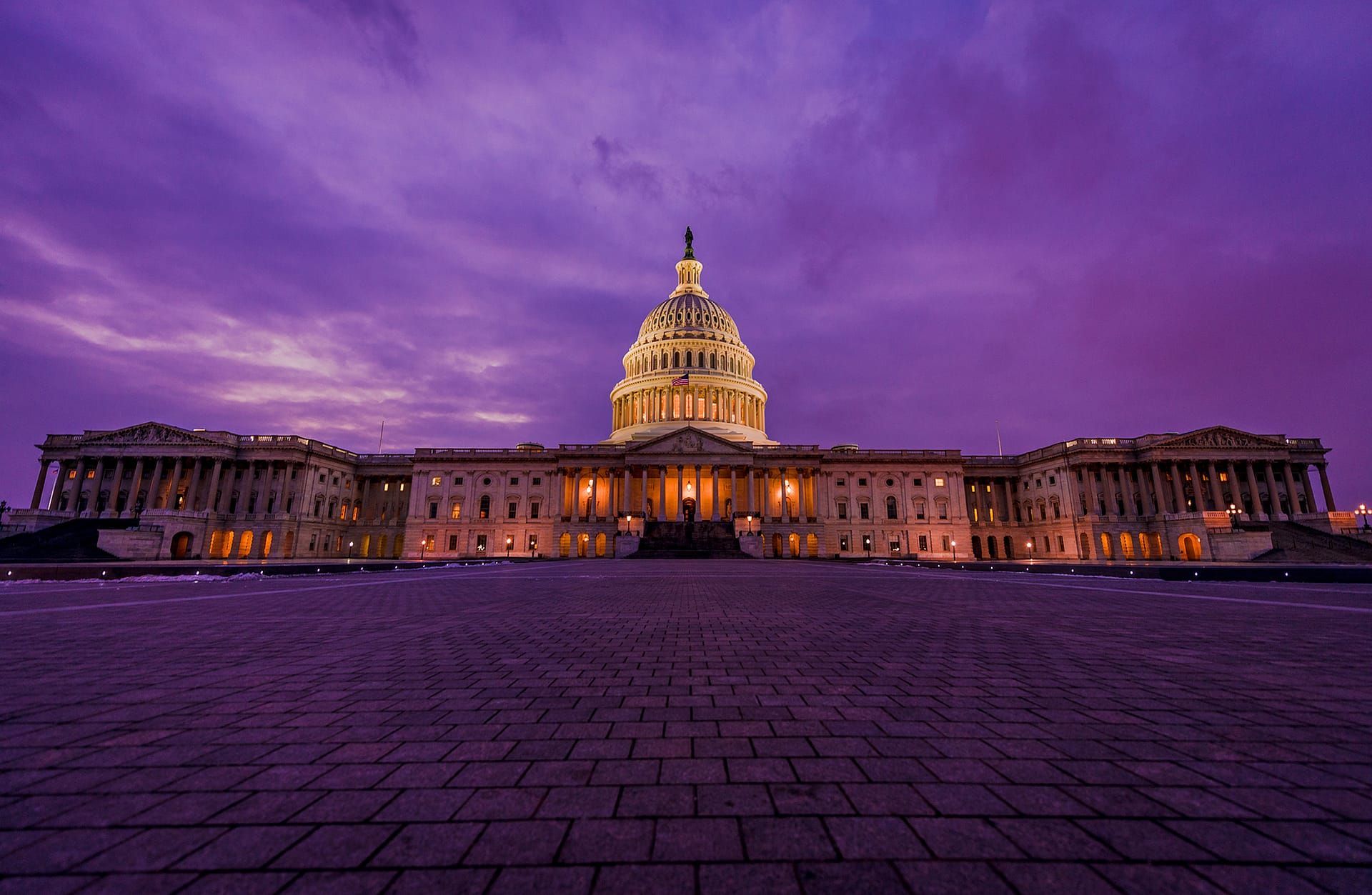 The capitol building is lit up at night with a purple sky in the background.