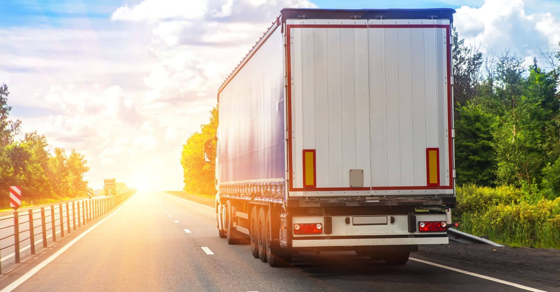 A semi truck is driving down a highway at sunset.