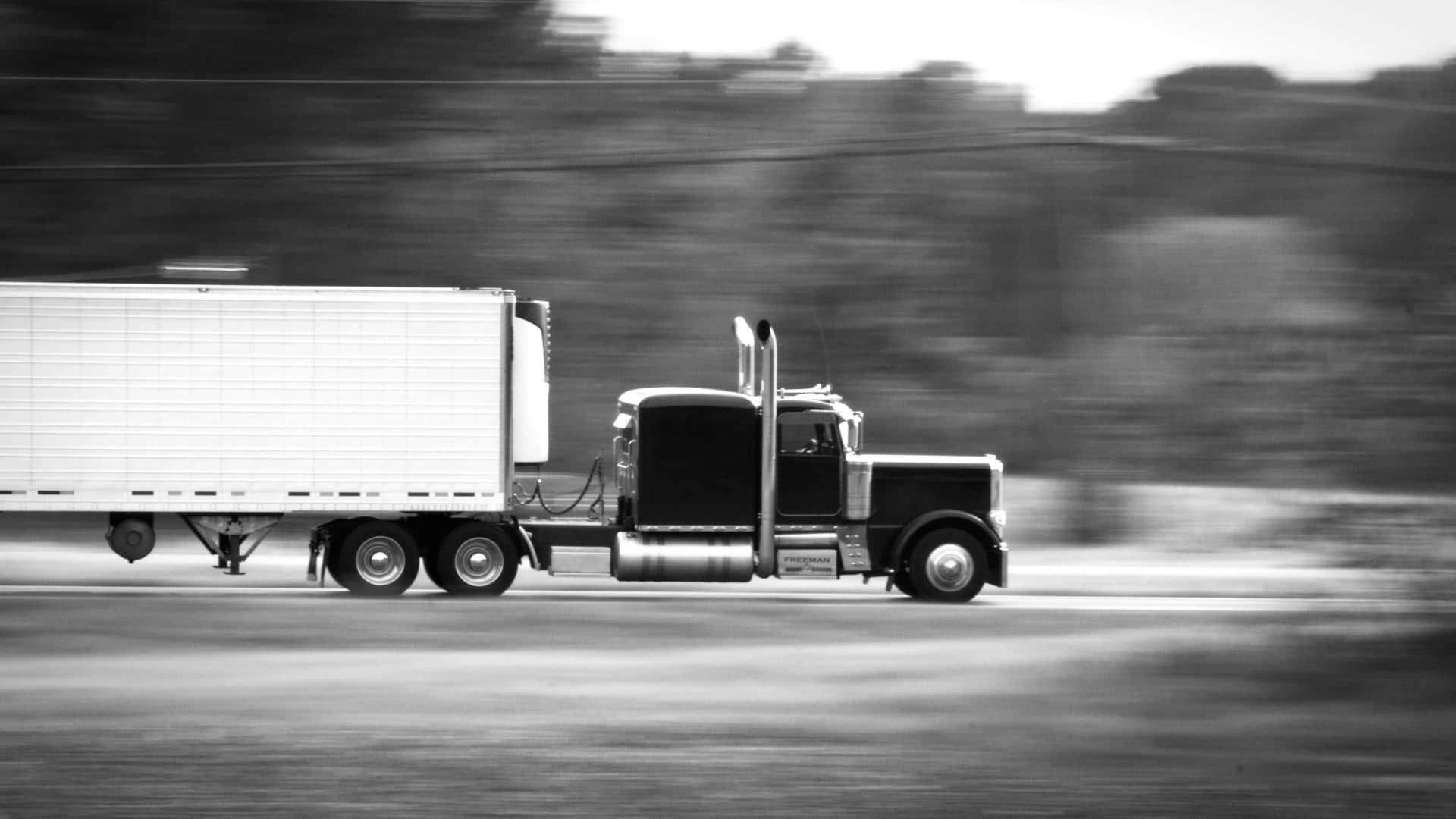 A black and white photo of a semi truck driving down a highway.