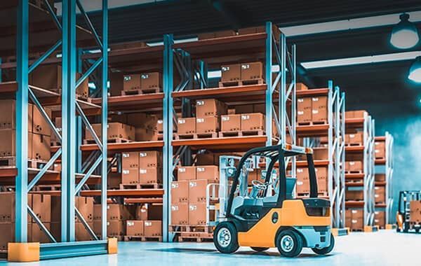 A forklift is driving through a warehouse filled with shelves and boxes.