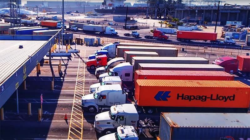 A lot of trucks are parked in a parking lot and one of them says hapag-lloyd