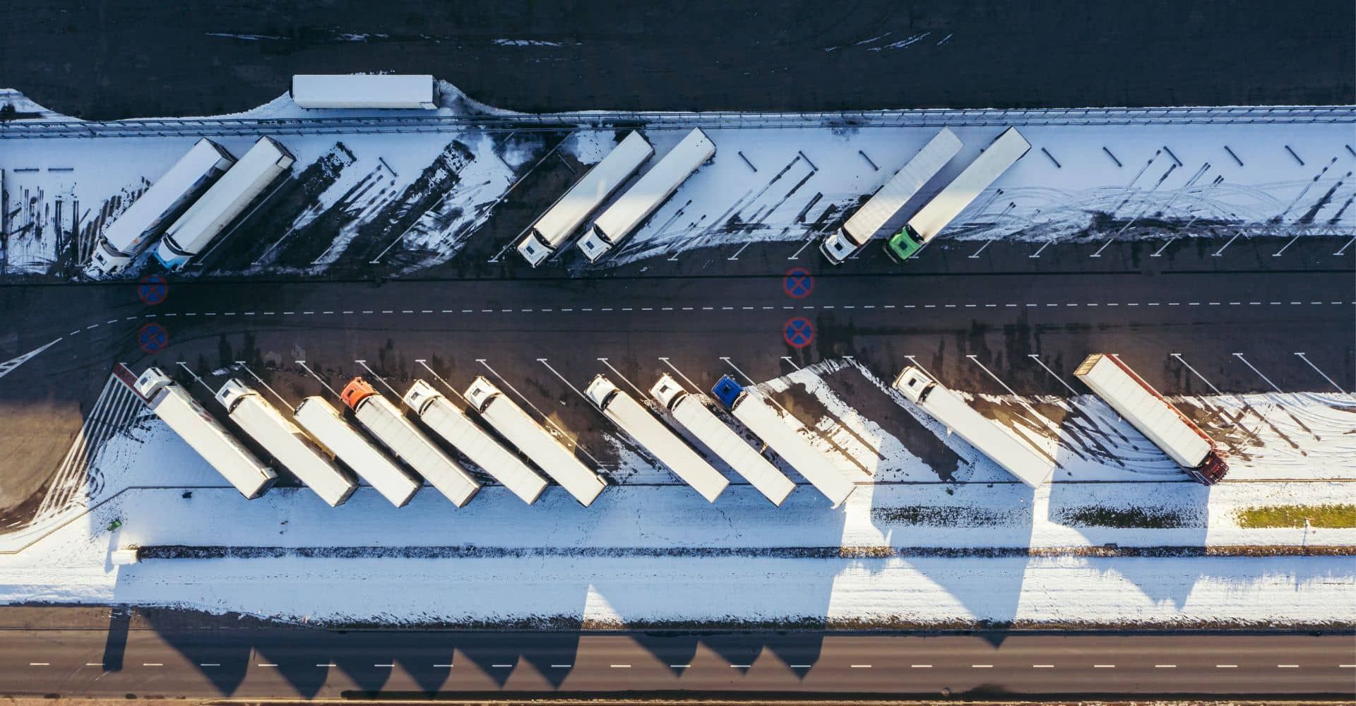 An aerial view of a row of semi trucks parked in a parking lot.