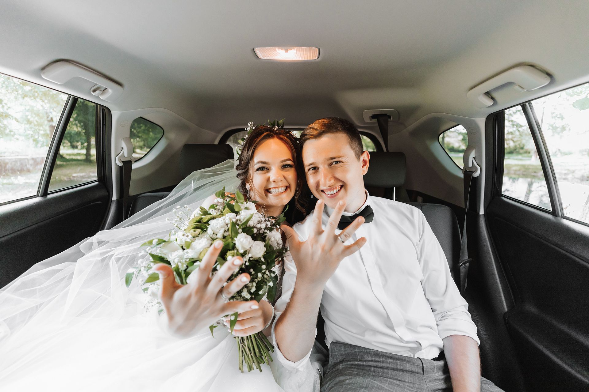 A bride and groom are sitting in the back seat of a car.