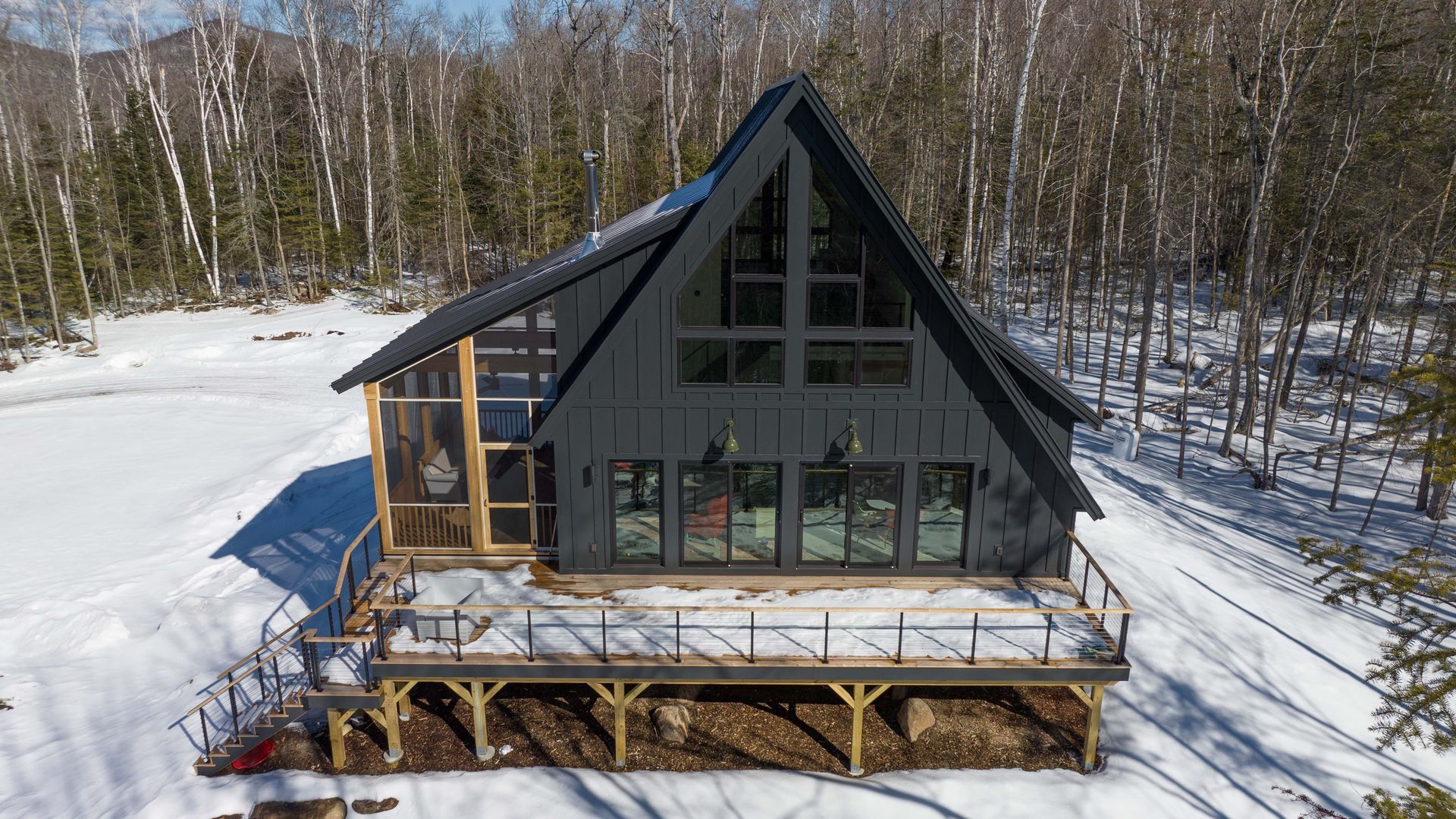An aerial view of a black house in the middle of a snowy forest.