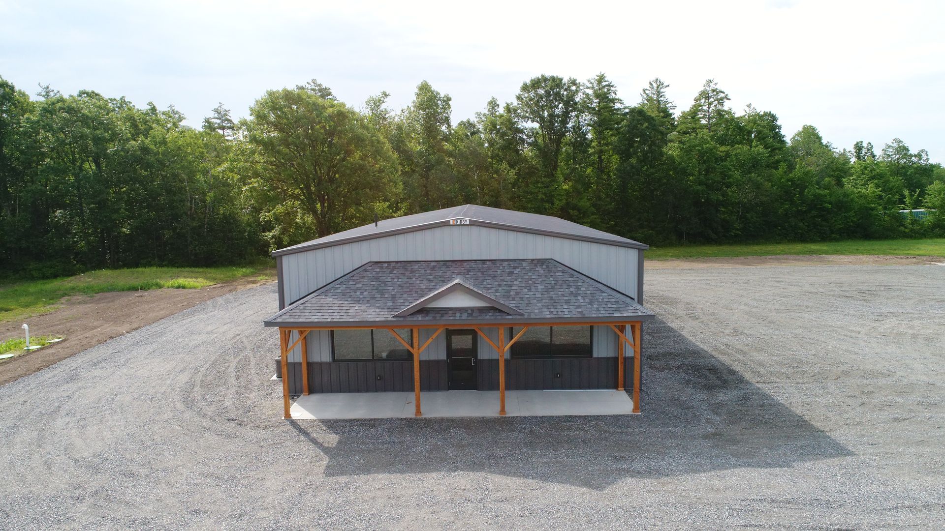 An aerial view of a building with a porch in a gravel lot.