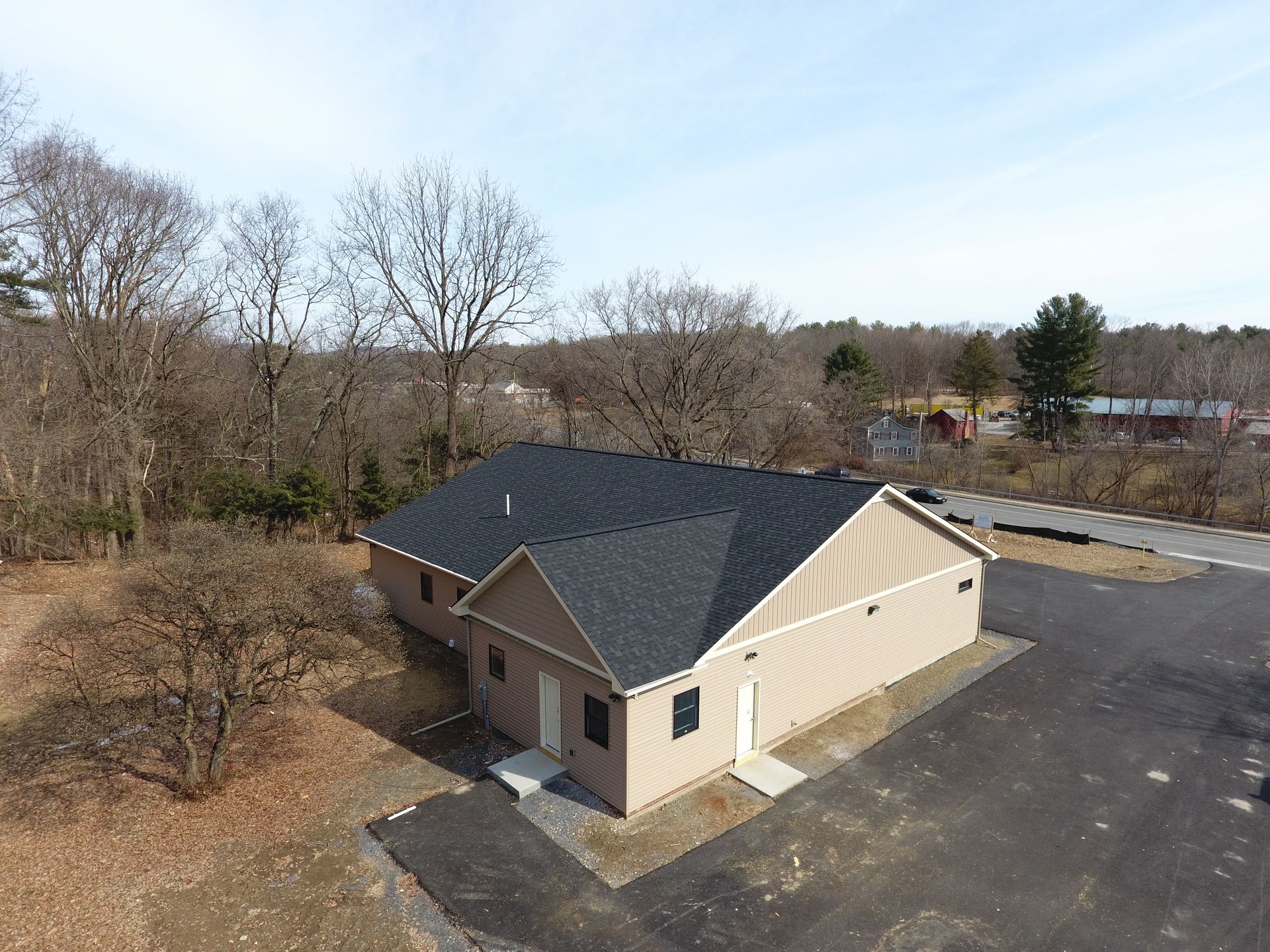 An aerial view of a house with a black roof in the middle of a forest.