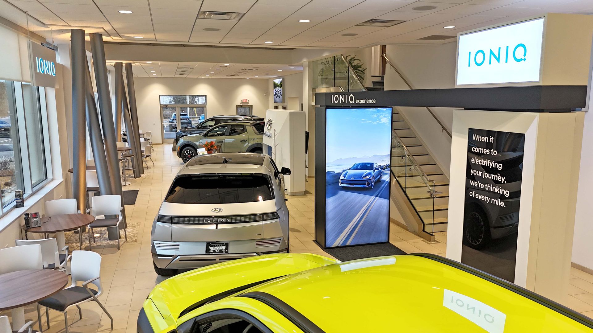 A yellow car is parked in a showroom next to a large screen.