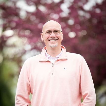 A bald man wearing glasses and a pink sweater is smiling for the camera.