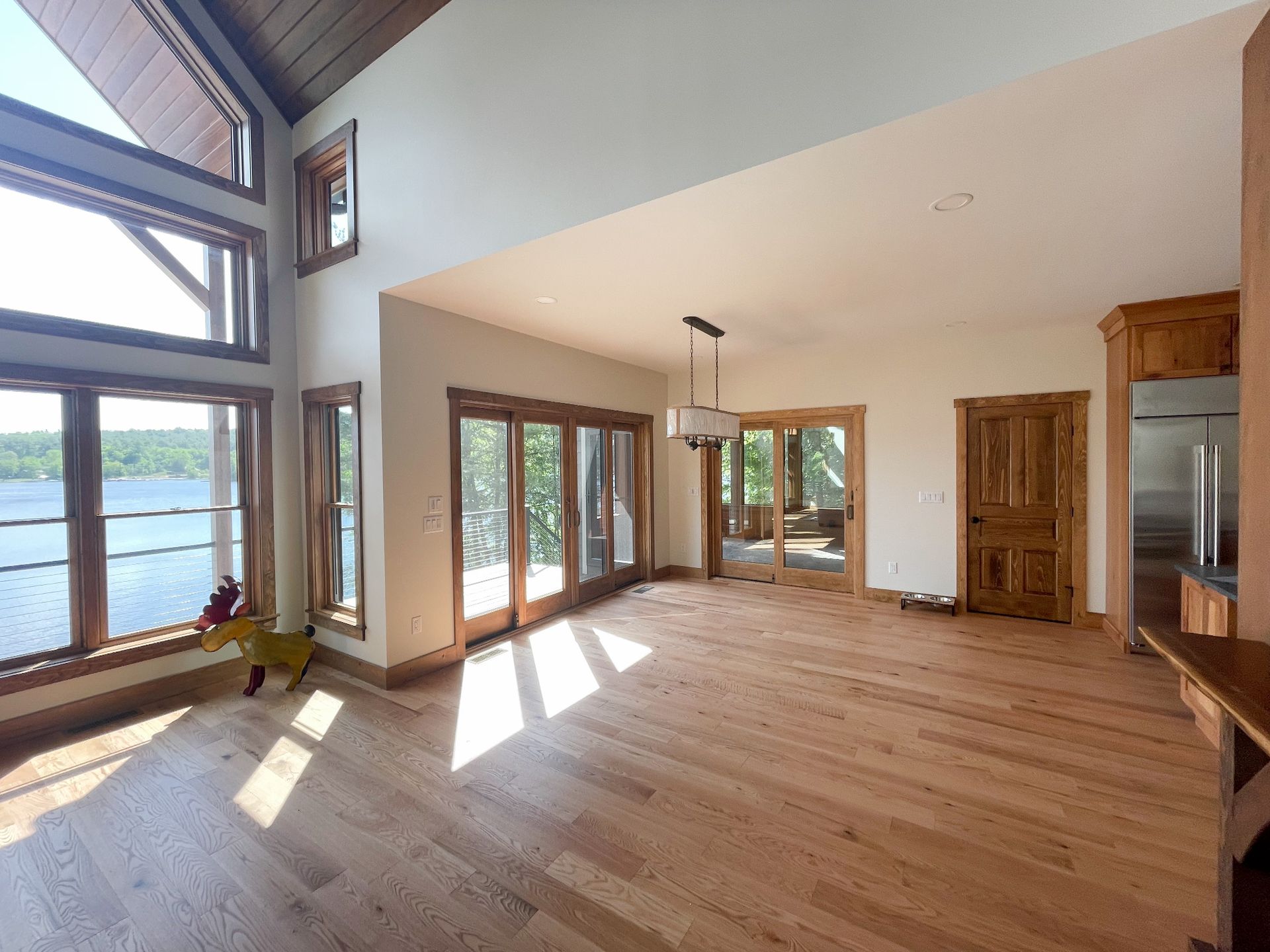 An empty living room with hardwood floors and lots of windows overlooking a lake.