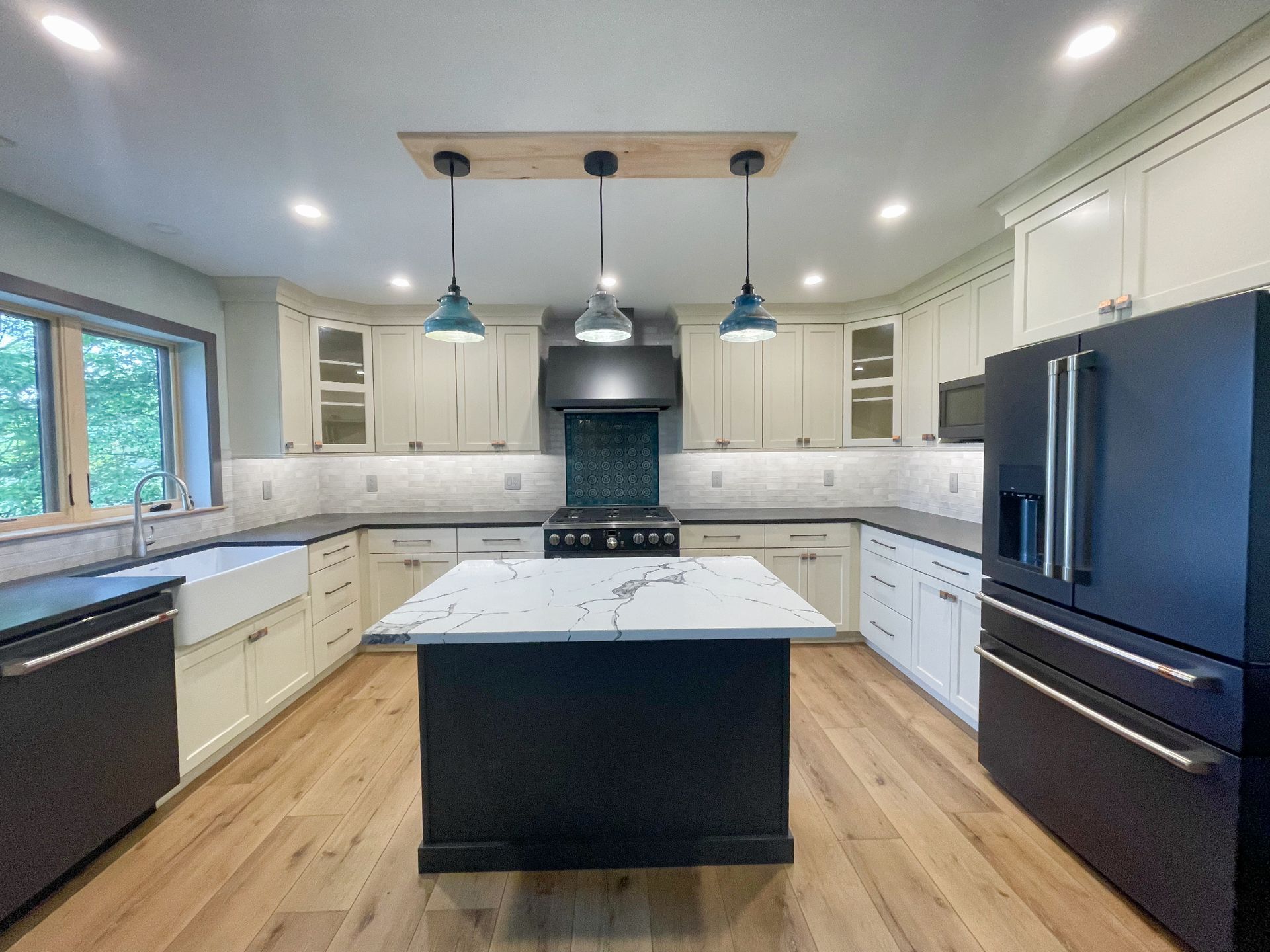 A kitchen with white cabinets and black appliances and a large island in the middle.