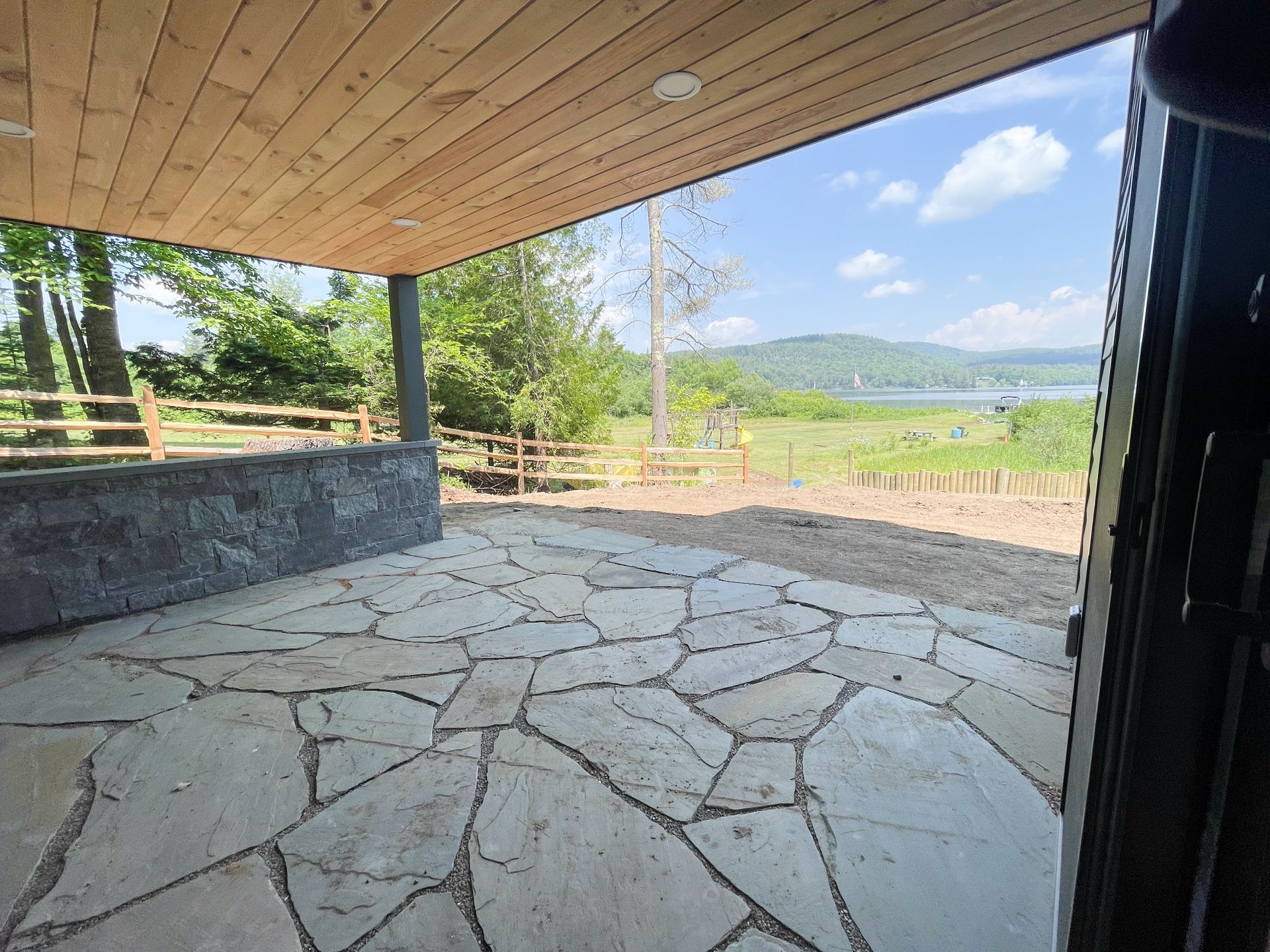 A stone patio with a wooden ceiling and a view of a lake.