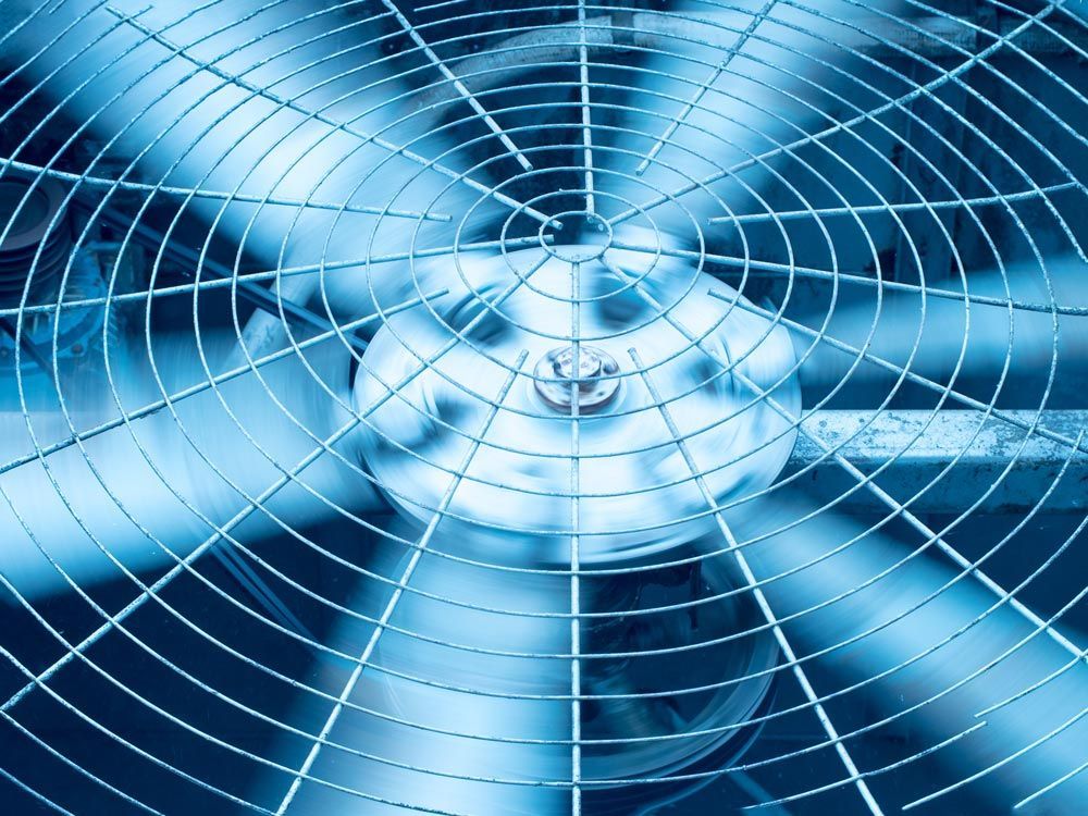 Close-up of a blue fan with a protective metal grill, blurring slightly as it spins.