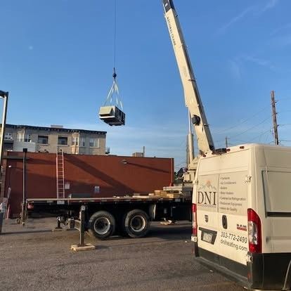 Two air conditioning units on concrete pads next to a building with a rock wall in the background.