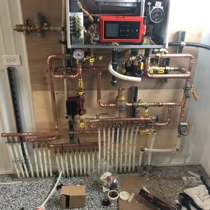 Copper pipes and heating system components mounted on plywood in a utility room.