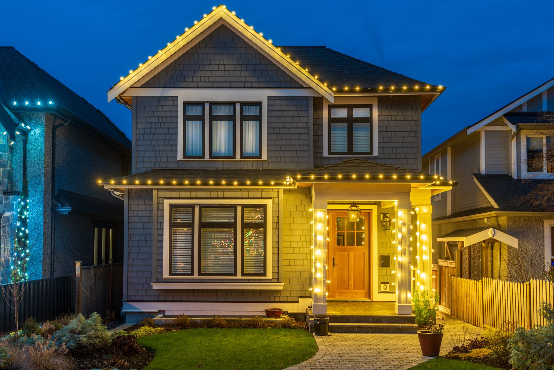 House decorated with green and white lights, with red trees in front. Night scene.