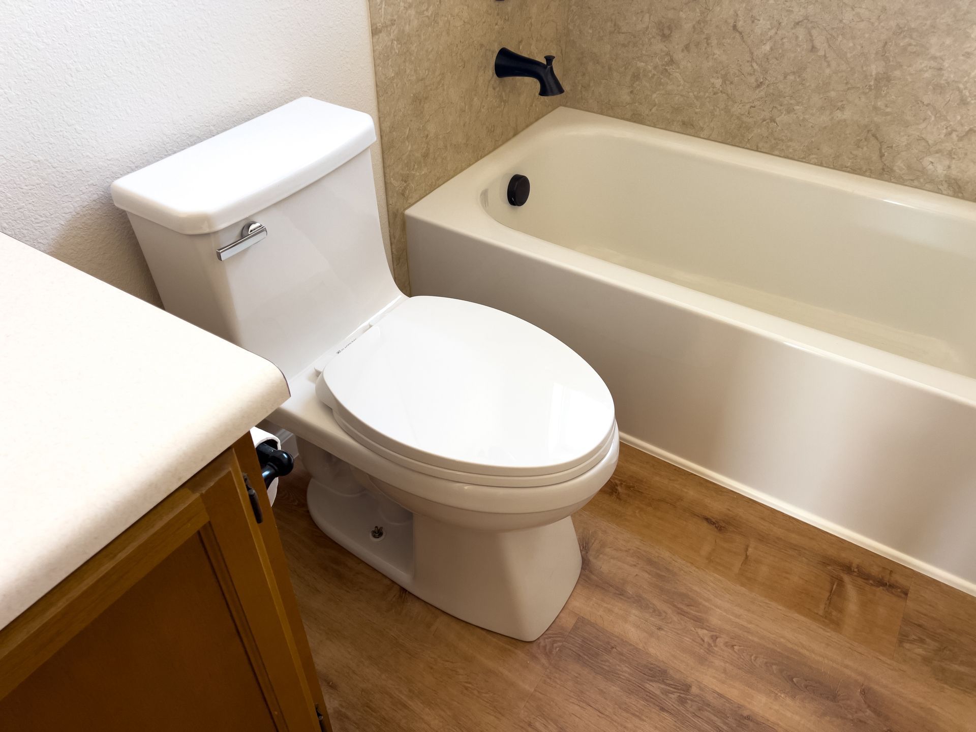 Bathroom with white toilet, tub, and wood-look floor; tan wall tiles.