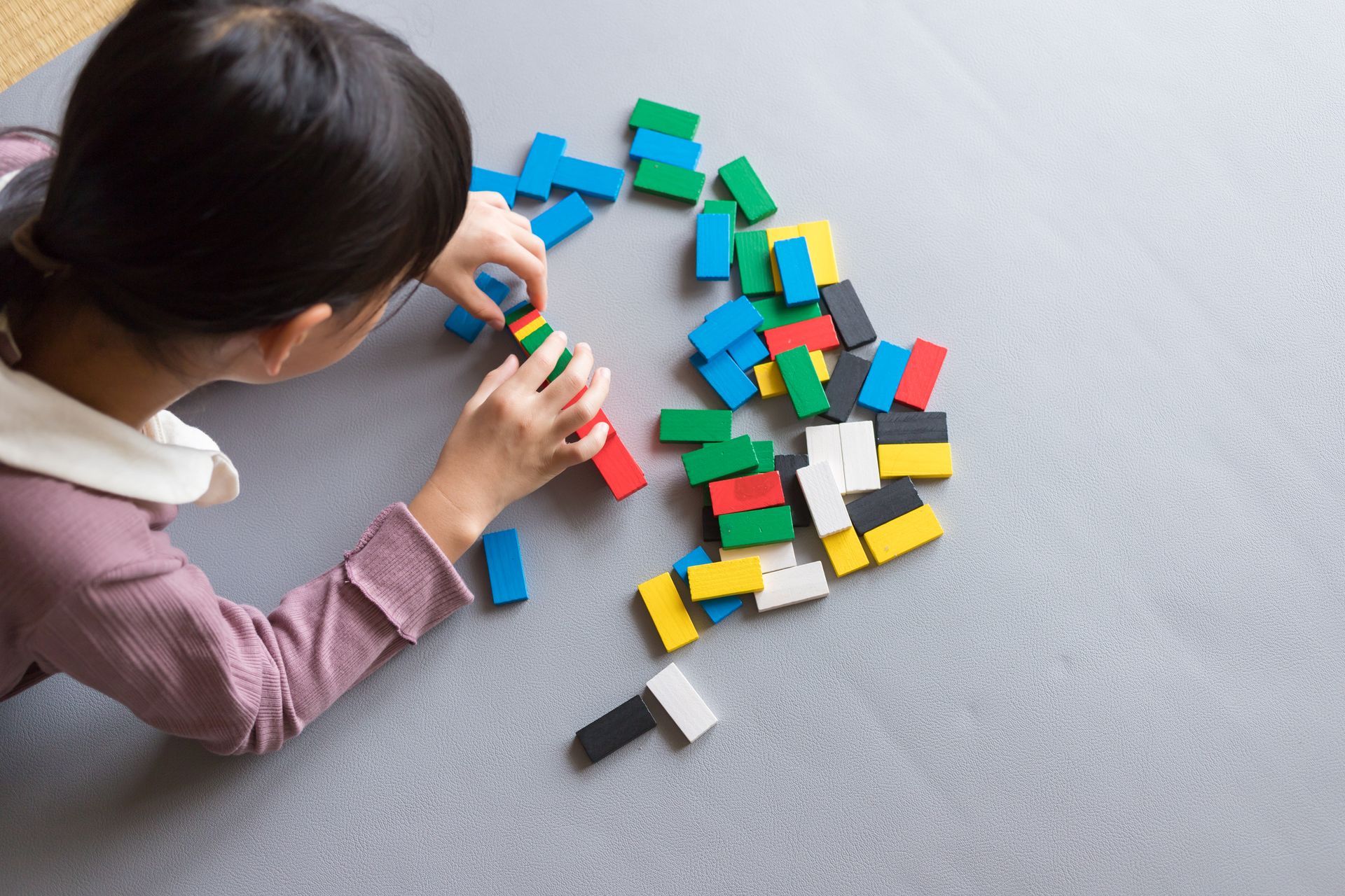 A little girl is playing with dominoes on the floor.