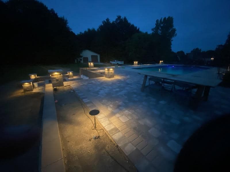 A patio with a swimming pool at night with lights on it.