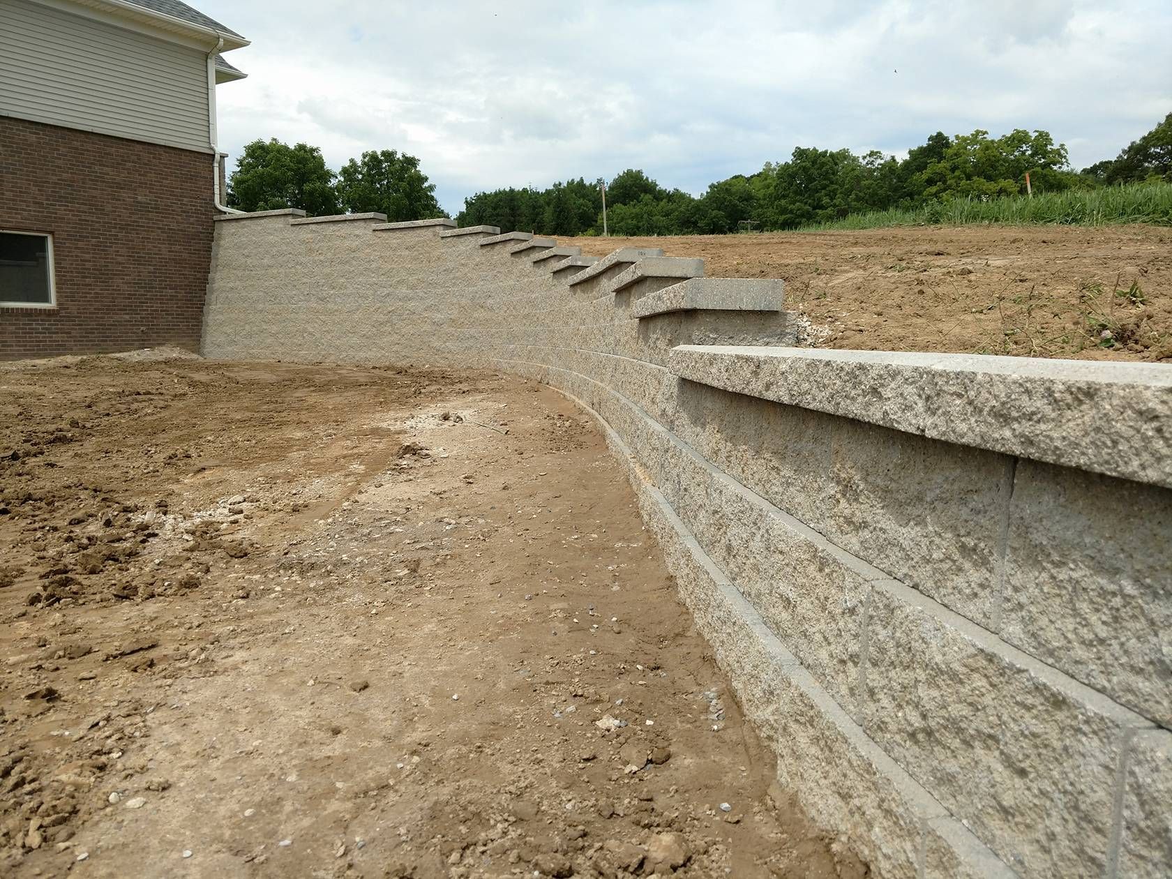 A brick wall surrounds a dirt field in front of a house
