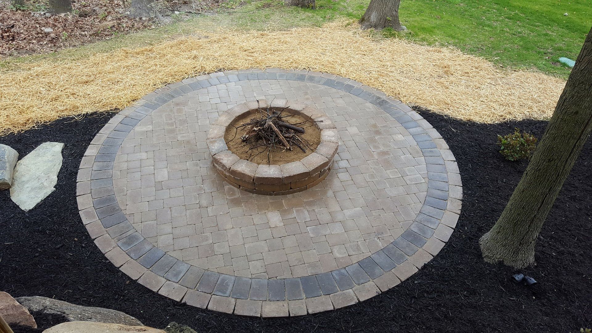 A fire pit is sitting in the middle of a circular brick patio.