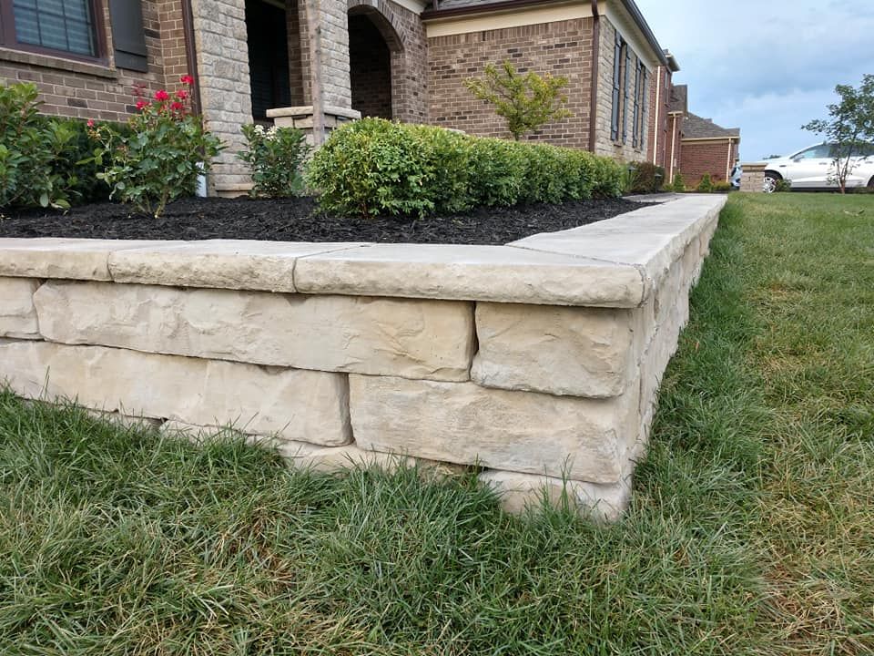 A stone wall is in the grass in front of a house.