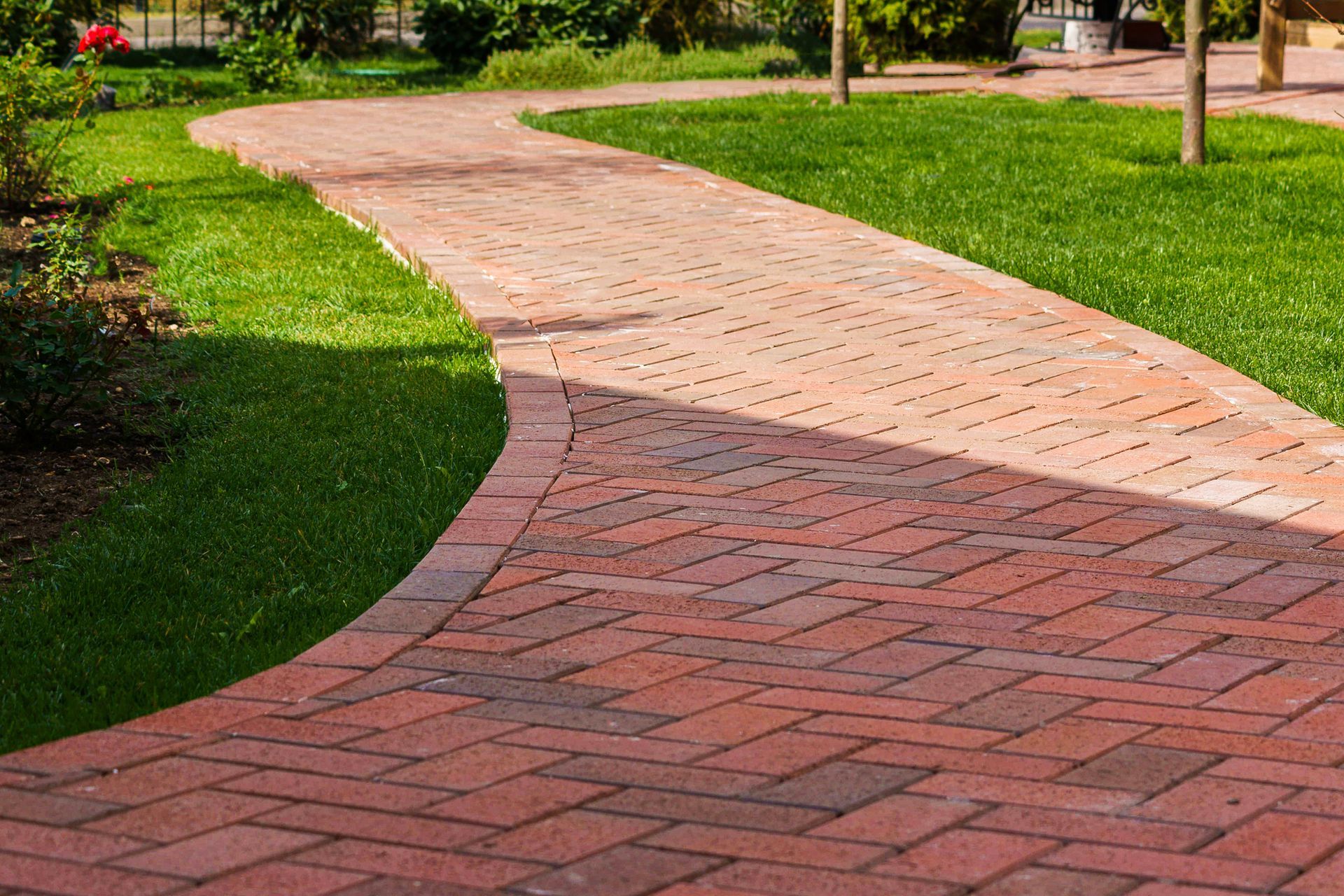 A brick walkway in a park surrounded by grass and trees.