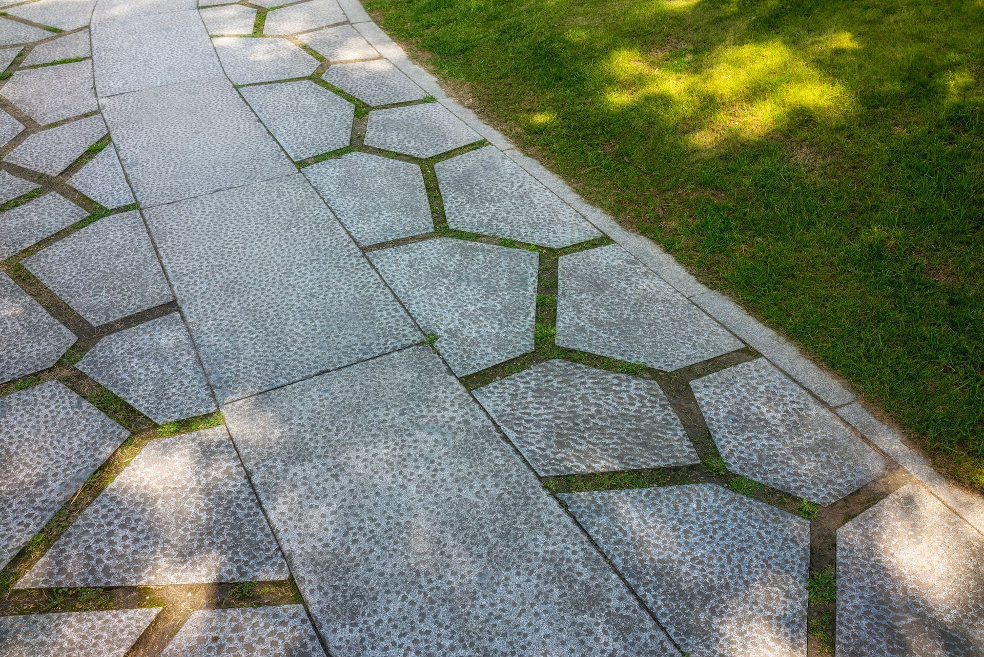 A stone walkway leading to a grassy area in a park.