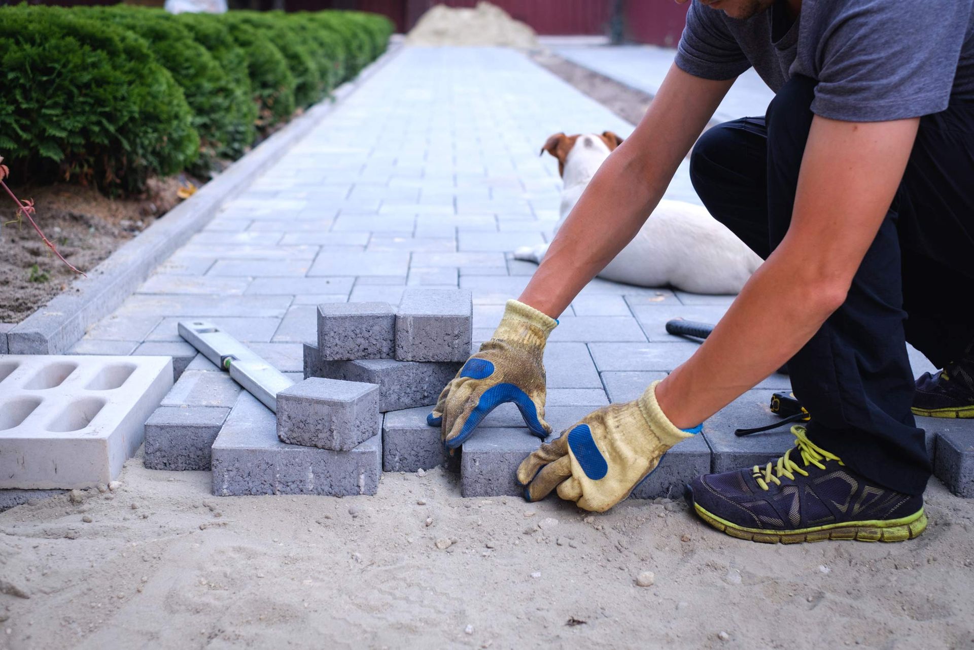 A brick paving contractor in yellow gloves lays paving bricks in Rochester, MI.