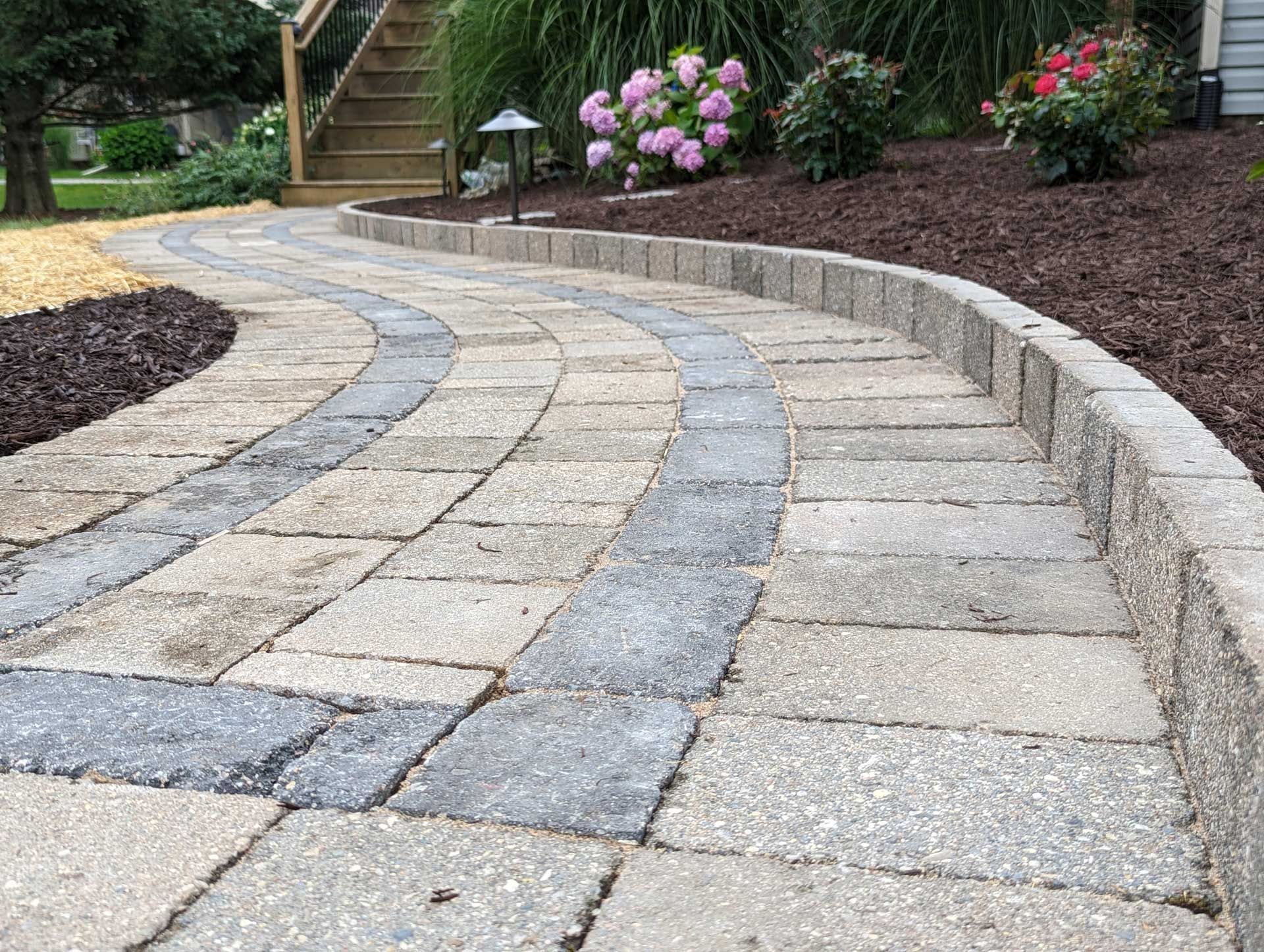 A curved brick walkway leading to a staircase in a garden.