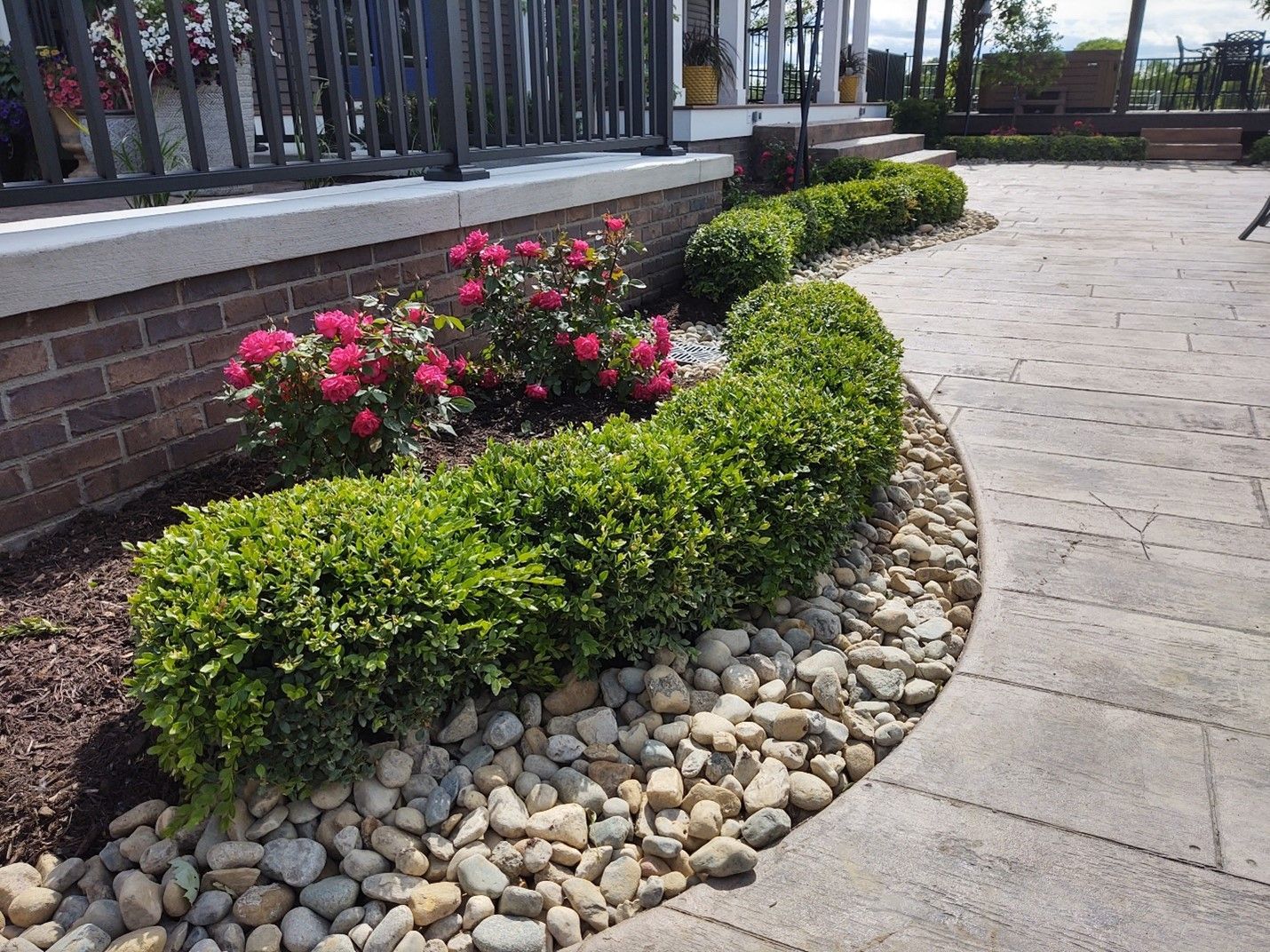 A patio with a brick wall , bushes , rocks and flowers.
