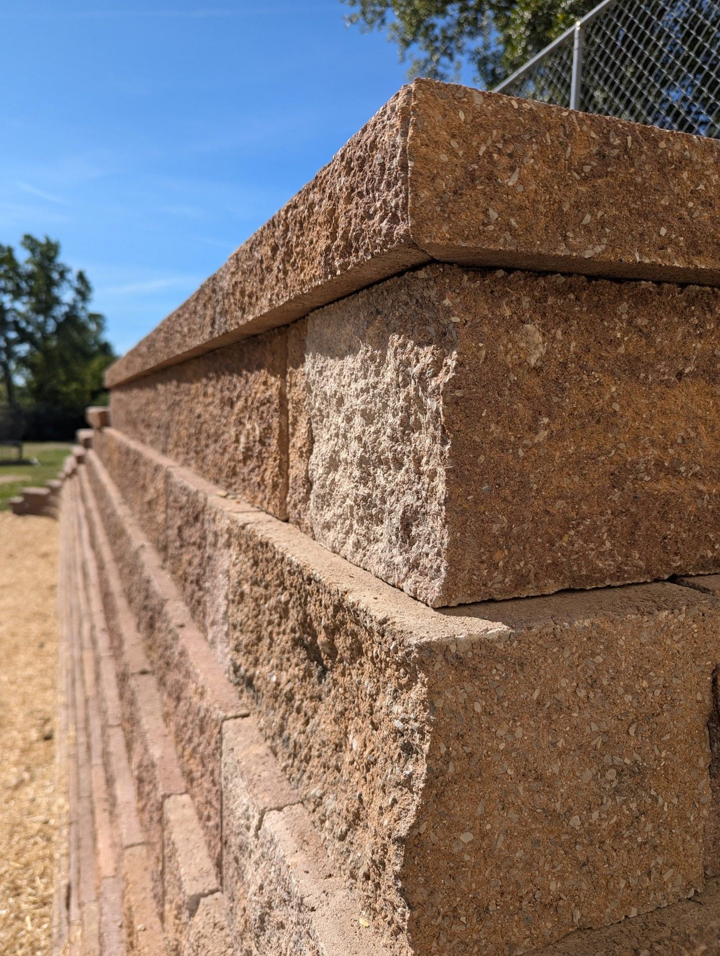 A brick wall with a chain link fence in the background
