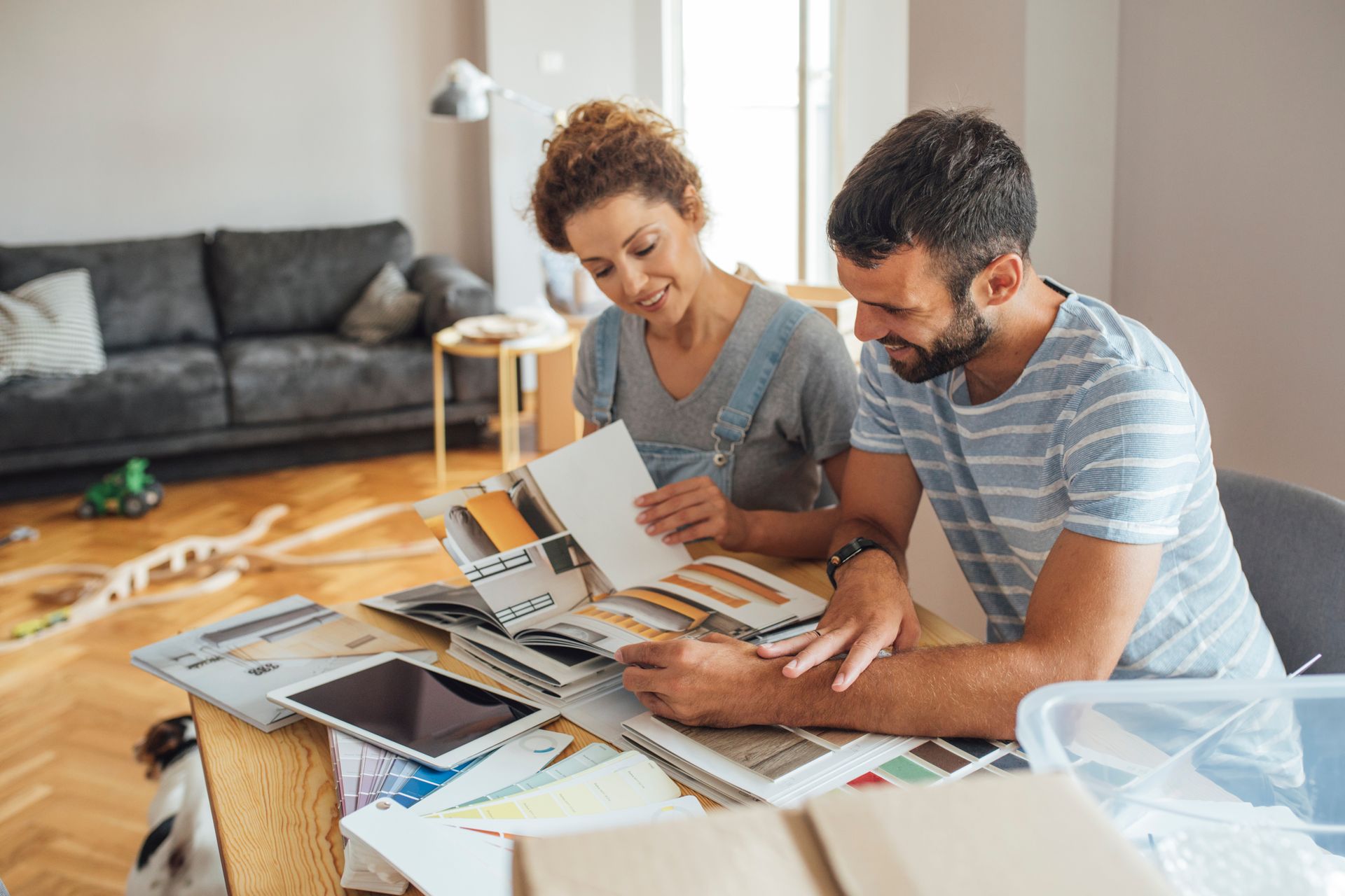 A couple sits at a table in a living room, reviewing fabric swatches and decor samples together while smiling.