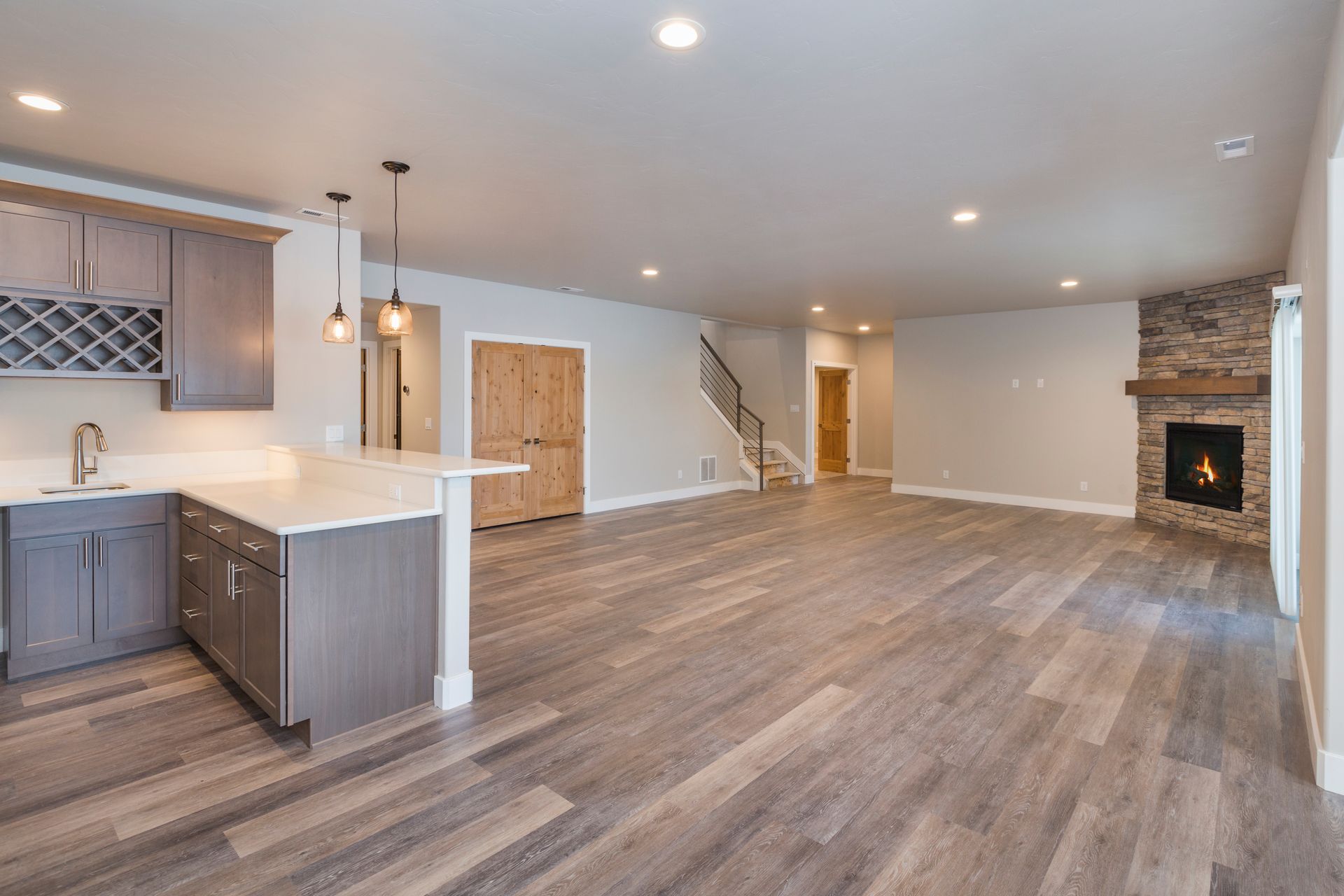 A spacious, modern open-plan living area featuring a kitchen with gray cabinets, wooden flooring, and a stone fireplace.